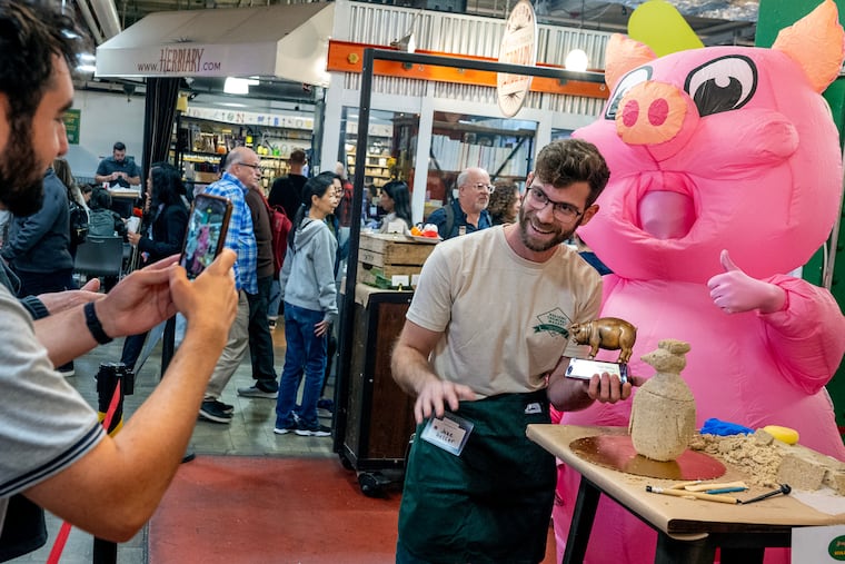 Jake Heller holds his pig trophy (named “Scrappy”) as he poses for a spectator with Filbert (the Market’s mascot) .after winning for his chicken vase (with a head that can taken off exposing a hollow body inside) at the Reading Terminal Market's inaugural Scrapple Sculpting Contest Thursday, Oct 10, 2024. A 5 lb block of scrapple and sculpting tools were provided to each contestant, with a professional artist judge selecting the winner. On Saturday during the Market’s Scrapple & Apple Festival another winner will be chosen by popular vote.