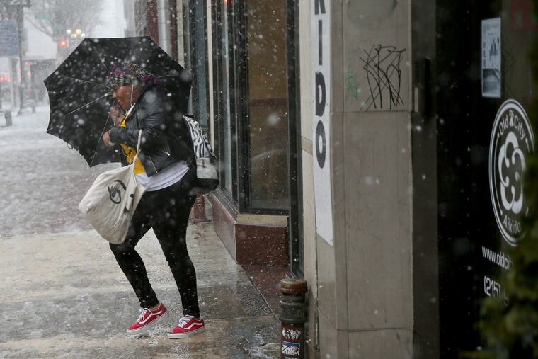 A woman’s umbrella is caught by strong winds along Market Street in Center City on Friday, March 2, 2018.