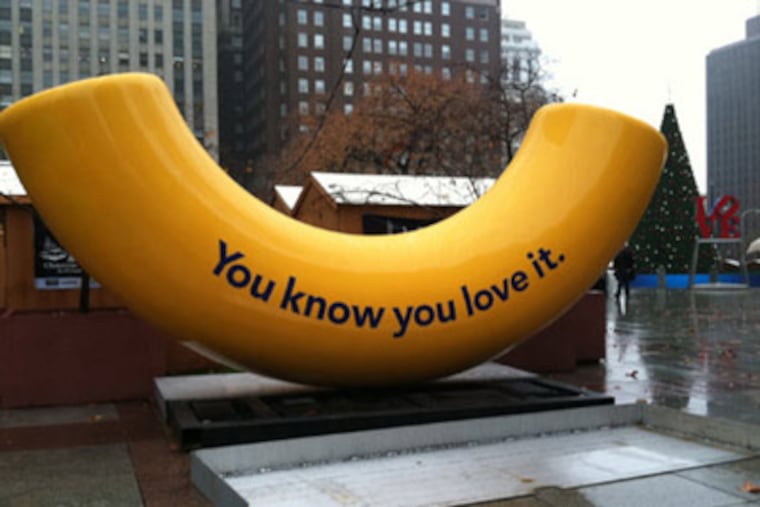 A giant yellow macaroni bearing a message from Kraft was installed in Love Park on Nov. 22, 2011. In the background are the shops of this year's Christmas Village, the Love sculpture and the city's holiday tree, which will be lit Dec. 7.