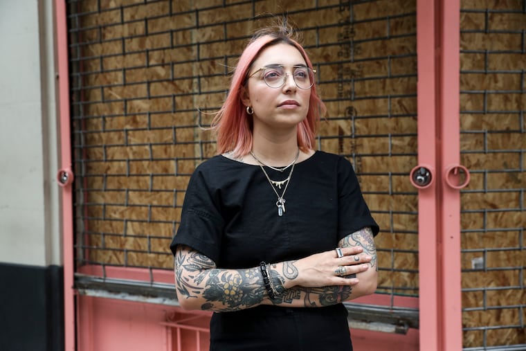 Angela Monaco stands outside her boarded-up shop, Ritual Shoppe, on Walnut Street in Center City. Even as Monaco struggled to remove items from her shop, the jewelry store was targeted by looters Saturday night.