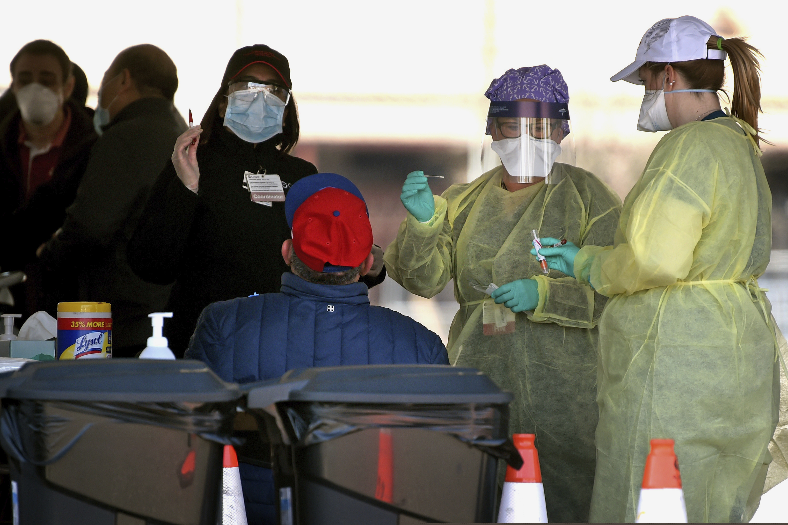 Medical workers from Cooper University Health Care and Virtua Health test Camden resident Antonio Rivera, in red cap, at the County's first public coronavirus drive-thru testing site at Cooper's Poynt Waterfront Park in Camden, N.J., Wednesday, April 1, 2020. He walked up to the site and was the first person tested.
