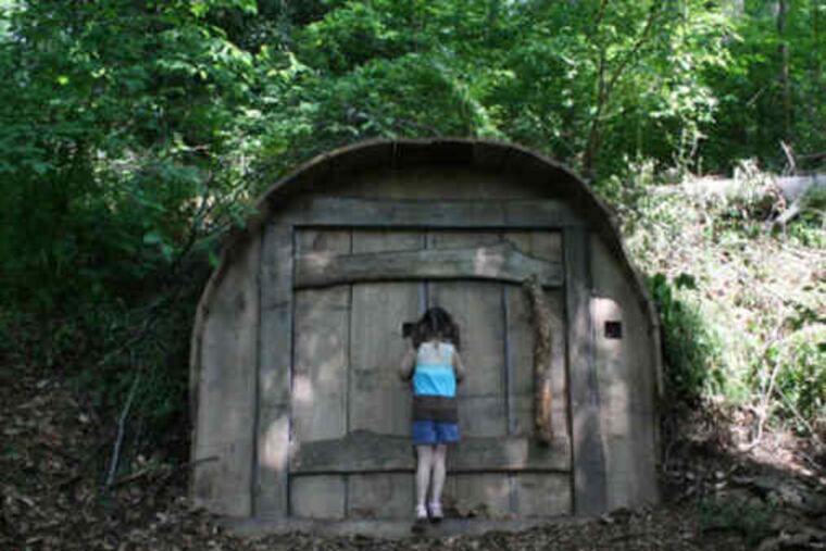 A girl peeks inside a giant wooden door called "What Lies Beneath?" The door is part of Nature's Enchantment, the newest exhibit at Tyler Arboretum, open through Oct. 31.