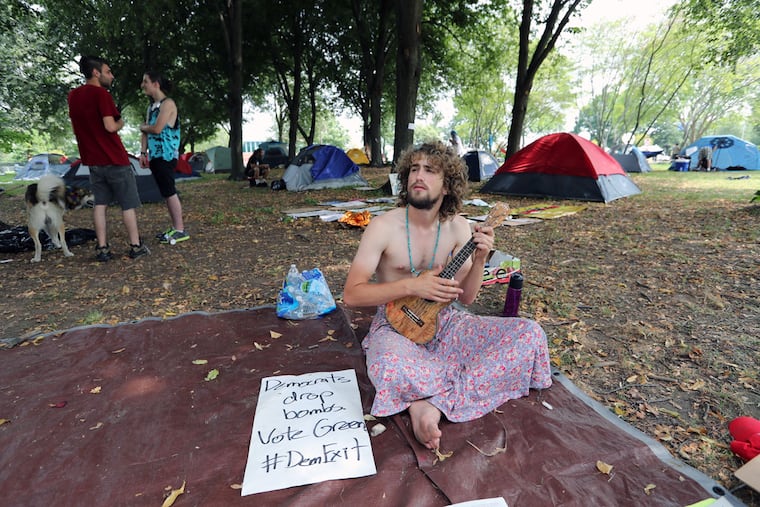 Tom Moore of Marion, Mass., wakes up with a tenor ukulele singing Bob Marley's "One Love" as dozens of protesters camp, sleep, meet and eat in FDR Park during the DNC at the Wells Fargo Center in Philadelphia.