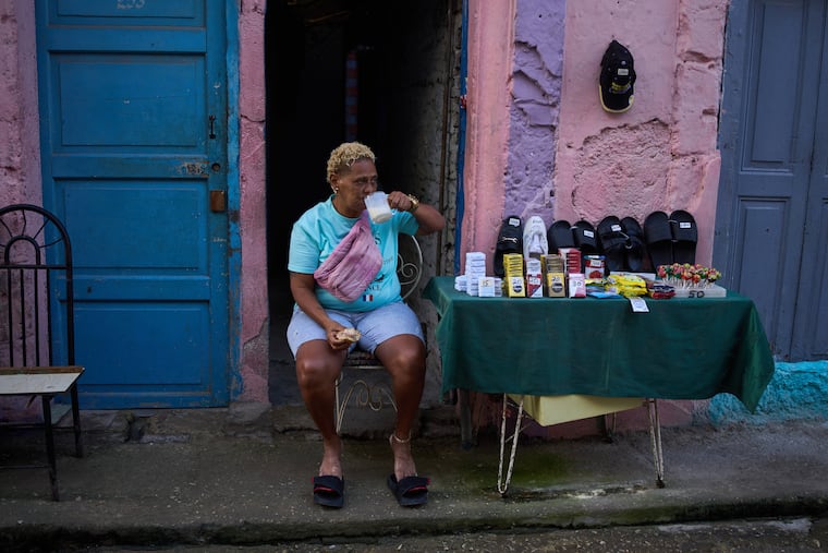 A vendor having breakfast sits by her table holding various products, from cigarettes to sandals, in Havana, Cuba, early Friday, March 13, 2026.