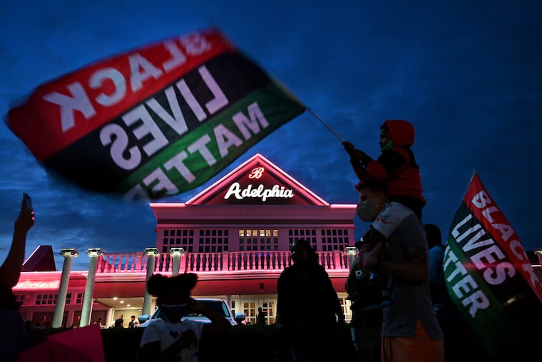 Zachariah Rattigan, 6, waves a BLM flag while sitting on the shoulders of his father, Bradley Pennypacker, of Woodbury, as they join other protesters gathered outside the Adelphia restaurant in Deptford on Aug. 4, 2021. They wanted an apology from the restaurant's owner after a Black man was bitten by a security guard dog.
