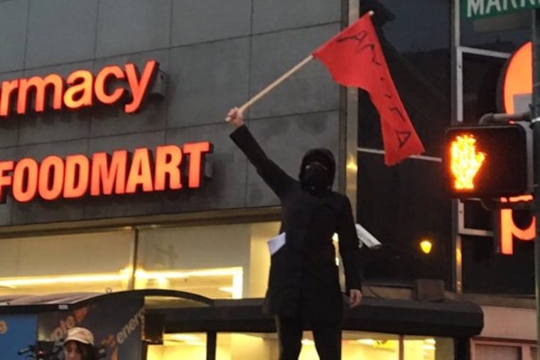 A masked, black-clad Antifa supporter waves a flag in Center City during President Trump’s visit in January.