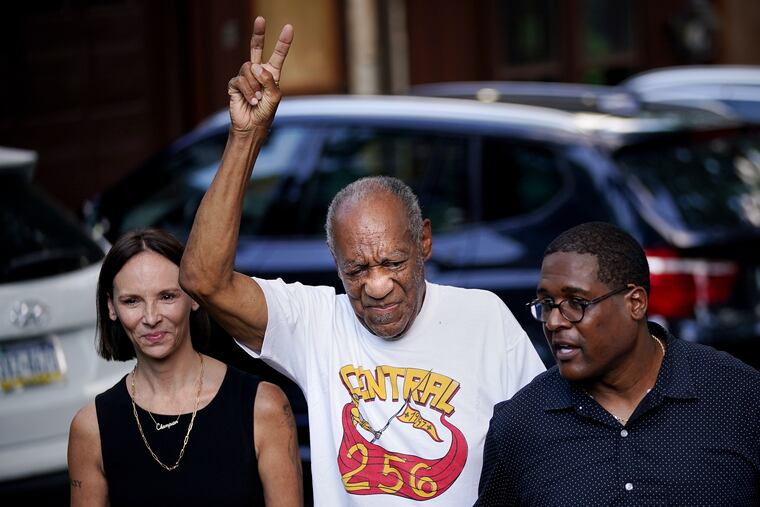 Bill Cosby (center), accompanied by attorney Jennifer Bonjean and spokesperson Andrew Wyatt, raises his hand as he makes his first public appearance at his home in Elkins Park after being released from prison several hours earlier on June 30, 2021. The Pennsylvania Supreme Court overturned Cosby's 2018 sexual assault conviction and ordered him released Wednesday.