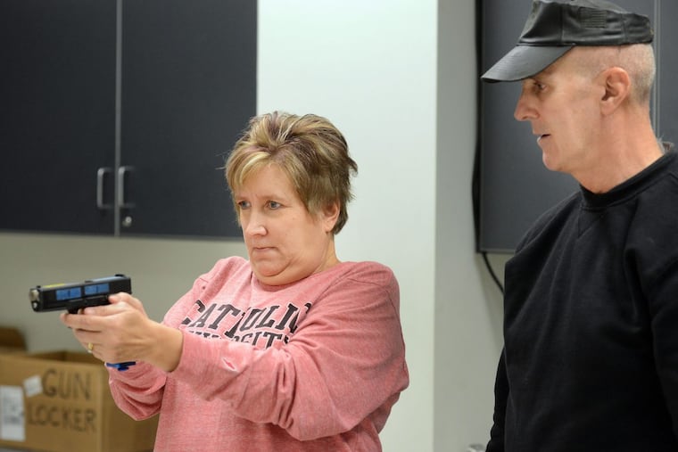 Officer Steve Dintino of East Pikeland Police (right) shows Nancy Griffith how to shoot a Glock training pistol in a shoot/don’t shoot simulation during the Citizens’ Police Academy at Chester County Intermediate Unit in Downingtown.
