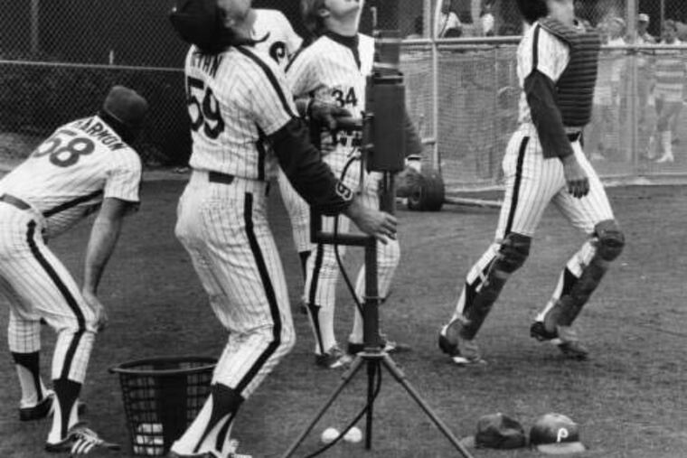Mike Ryan using machine to shoot balls in the air while catcher Bob Boone sets to catch them and other catchers watch, 1979.