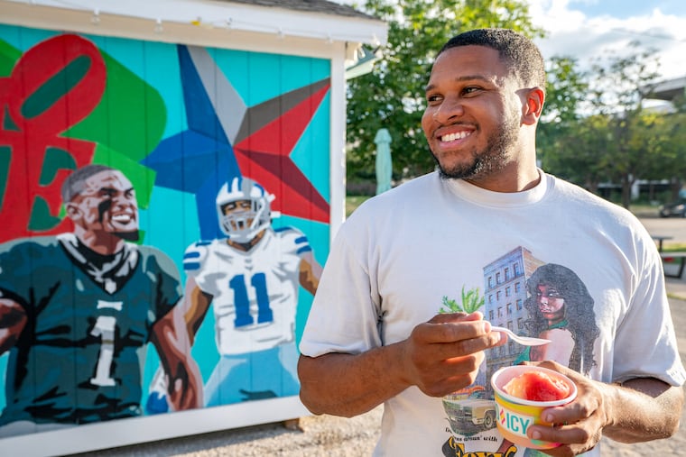 Bruce Mapp, 31, poses with water ice in front of the mural of Eagles quarterback Jalen Hurts and Cowboys linebacker Micah Parsons that adorns one of his ice stands in Dallas.