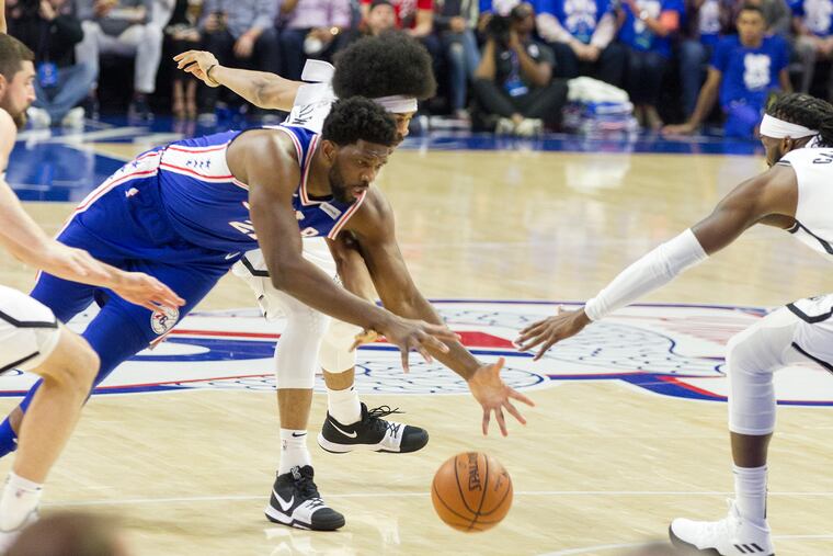 Joel Embiid, left, of the Sixers dives after a loose ball against Jarrett Allen, center, and DeMarre CArroll of the Nets during the 1st half of their NBA playoff game at the Wells Fargo Center on April 13, 2019.