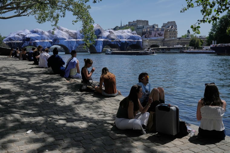 People seek relief from the heat along the Seine River in Paris, Monday, May 25, 2026. Artwork by street artist JR is seen on the Pont Neuf in the background.