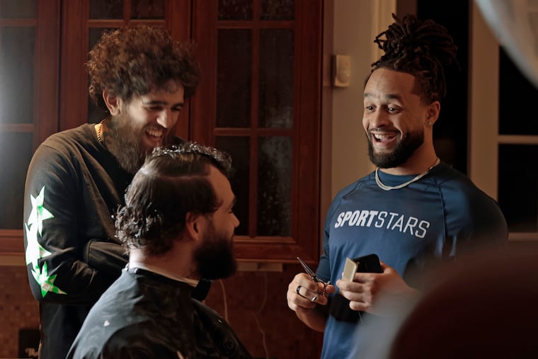Eagle's safety Avonte Maddox (right) smiles after telling teammate Dallas Goedert (seated) that he just cut a small bit of Goedert's hair. Goedert was getting a trim and haircut from No Push Backs barber Tony Saunter (left) at Maddox's South Jersey home on Sat., Feb. 04, 2023.