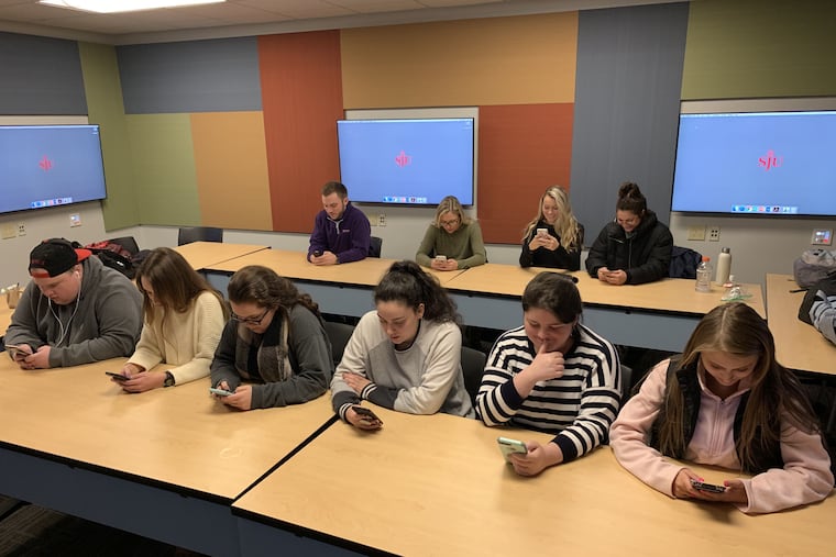 These undergrads at St. Joseph's University, pictured staring at their cells, gave up their smartphones for a day in January 2019, as an assignment for their professor, Inquirer columnist Maria Panaritis. What they discovered wasn't pretty.