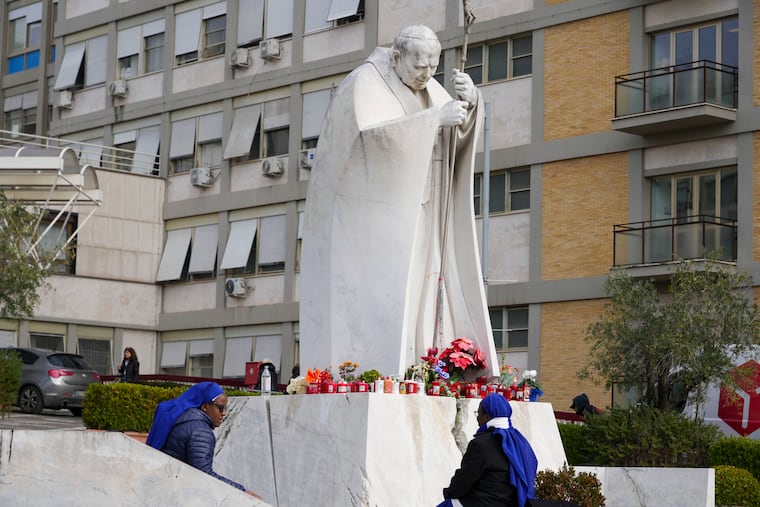 Nuns sit next to a statue of Pope John Paul II in front of the Agostino Gemelli Polyclinic in Rome, where Pope Francis has been hospitalized, on Monday, Feb. 17, 2025.