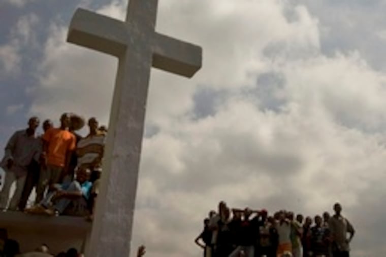 A man stands atop Baron Samedi's cross at Petionville Cemetery in Port-au-Prince. Millions of Haitians practice Voodoo, a blend of Christian tenets and African religions created by slaves.
