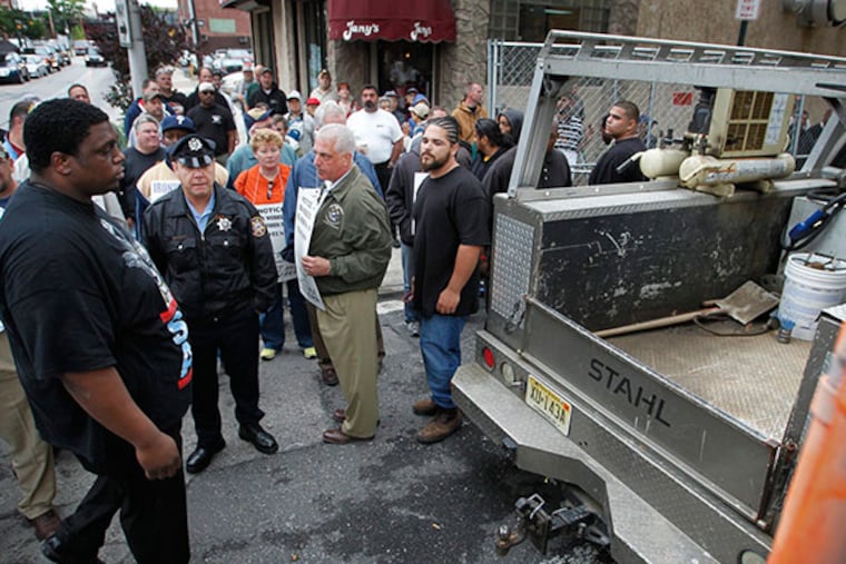 An employee of the Post Brothers construction, left, escorts a work vehicle to the job site as protestors stand in the background. ( ALEJANDRO A. ALVAREZ / STAFF PHOTOGRAPHER )