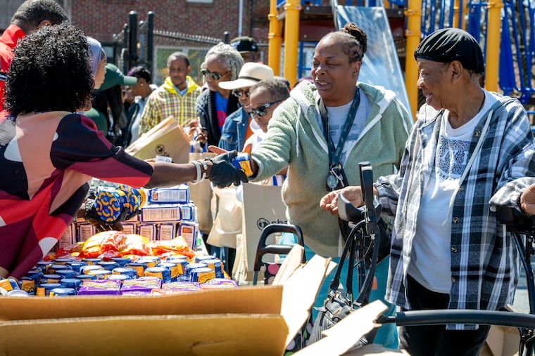 Casandra Harris and her mother, Willie Harris (right), accept food from Mayor Cherelle L. Parker as she helps distribute mac and cheese at a neighborhood food drive Sunday, April 12, 2026, for residents impacted by the collapse of the nearby parking garage. Demolition and recovery efforts for two ironworkers' bodies continued in Grays Ferry.