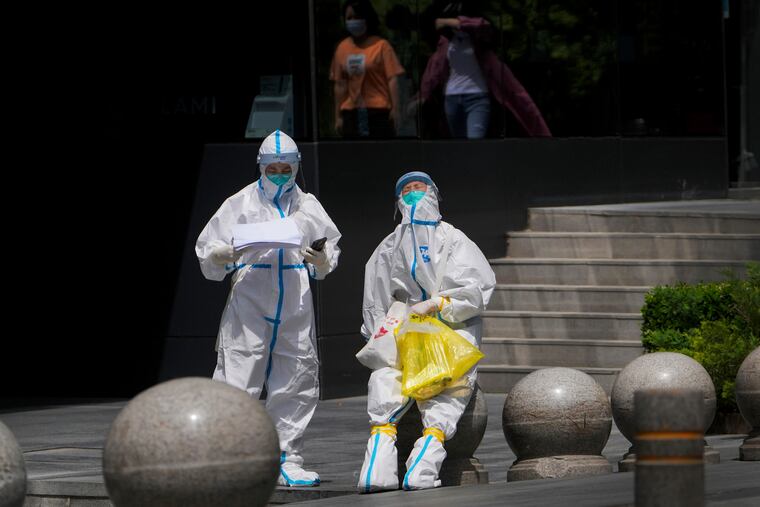 Medical workers in protection suits take a rest after conducting COVID tests for residents near a commercial office complex Thursday in Beijing.