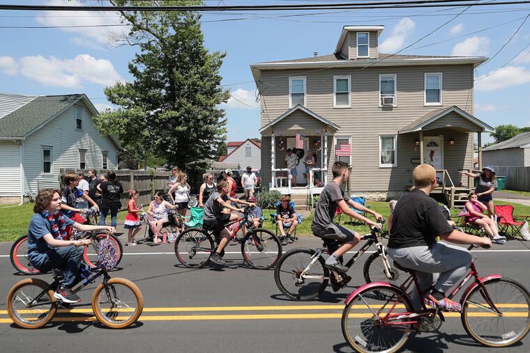 Participants bike along State Road during the Memorial Day parade in Croydon, Bucks County, as spectators watch from the roadside and front porches.