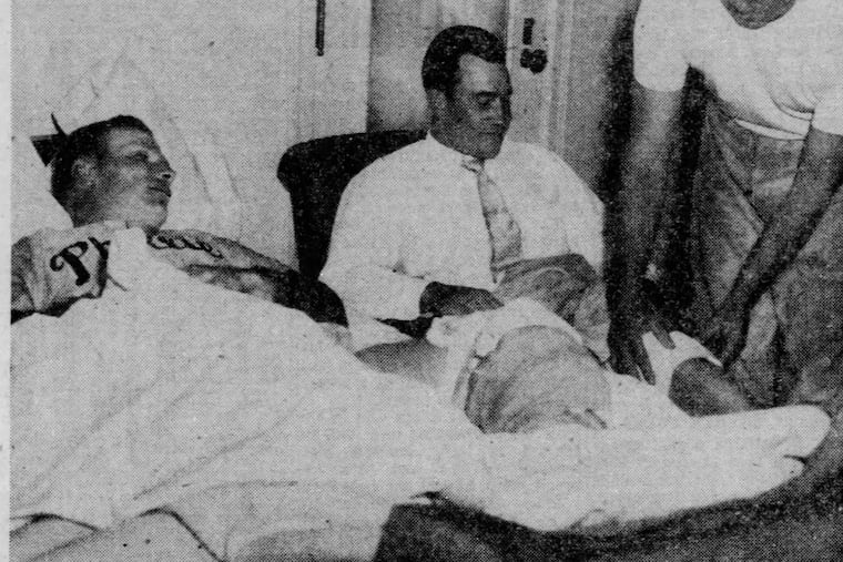 Richie Ashburn (in bed with a bandaged left knee) watches Phillies trainer Frank Wiechec put another bandage on Del Ennis' left knee in Richie's room in the Hotel duPont in Wilmington, Del. The outfielders collided in the eighth inning of a spring training game on April 8, 1955 against the New York Yankees.