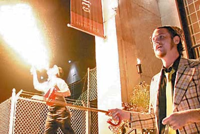 John Peterson entices people to step inside to watch the Olde City Sideshow while Martin Stutzman breathes fire. (Robert Moran / Inquirer)