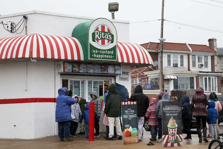 Customers wait in line amid snow and freezing rain for free ice to celebrate the first day of spring at Rita's Water Ice in Olney on Tuesday, March 20, 2018.
