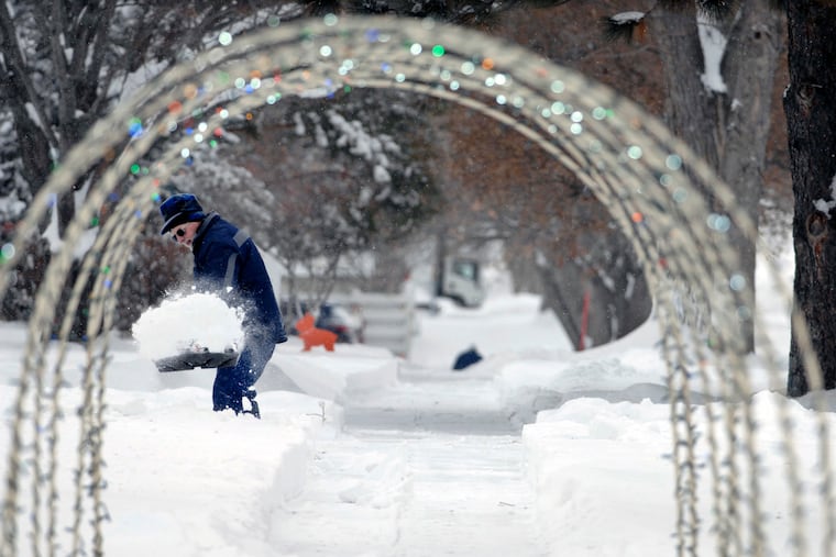 A Christmas outdoor decoration placed over a sidewalk frames a man shoveling snow after a holiday-week storm in Bismarck, N.D. in 2018.