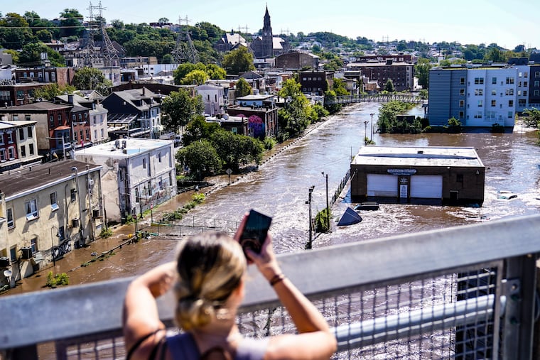 A person takes a photo of the Schuylkill River after it flooded the Manayunk section of Philadelphia in the aftermath of Hurricane Ida on Thursday Sept. 2, 2021.