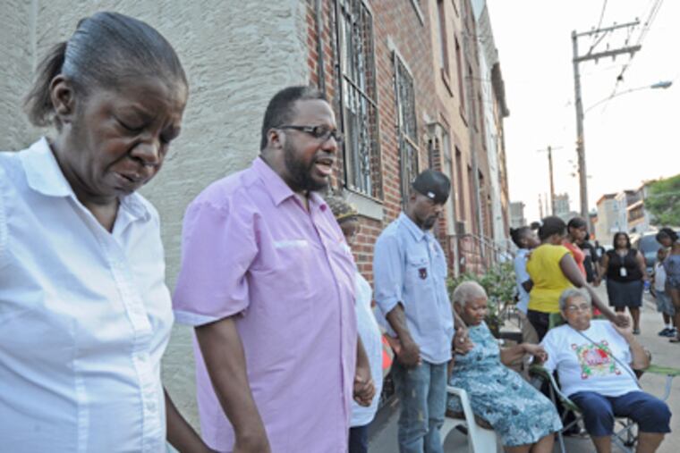 On West York Street in North Philadelphia, friends of James "Bus" Hall pray. At left is Hall's girlfriend, Juanita Johnson; next to her is Pastor Glenn Dawson of the Evangelistic Temple Worship Center. (April Saul / Staff Photographer)
