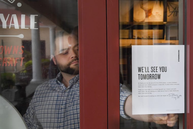 A Starbucks staff member tapes a message to the door of a Starbucks on Bala Cynwyd, letting customers know that the store will be closed the rest of the day on Tuesday.
