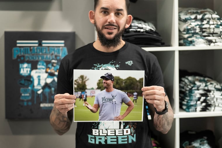 Jay Pross holds a photo of Eagles coach Nick Sirianni wearing one of his designs for sale at his clothing store, Art History 101 Clothing Co. Art History burned down two years ago. Now, Sirianni is wearing the company's T-shirts.