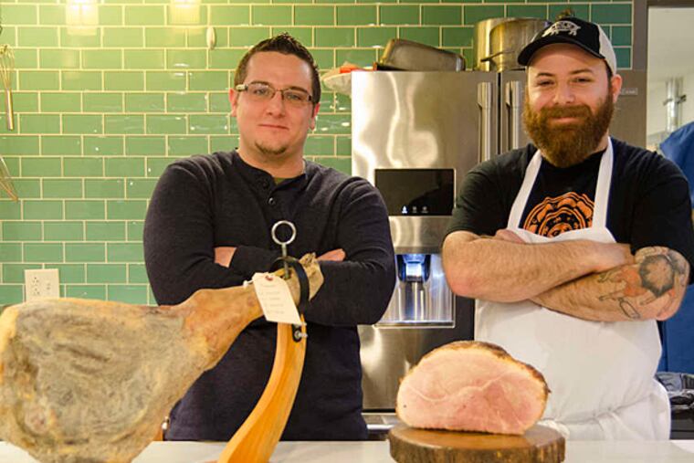 Chefs Tony Page (left) and Nick Macri serve a keystone cured ham (left) and a slow roasted ham as part of an Easter spread in the Reading Terminal Market test kitchen. (RACHEL WISNIEWSKI / Staff Photographer)