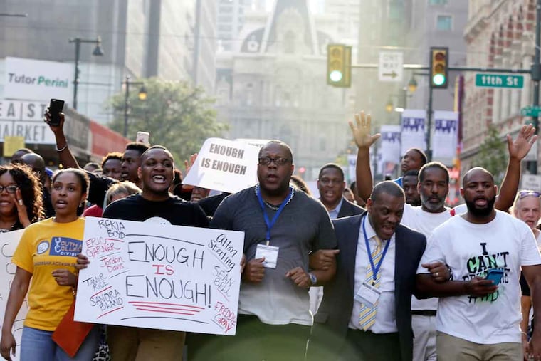 In Center City, protesters link arms and hold signs while marching along Market Street. Clergy members and Black Lives Matter activists organized Thursday’s demonstration.