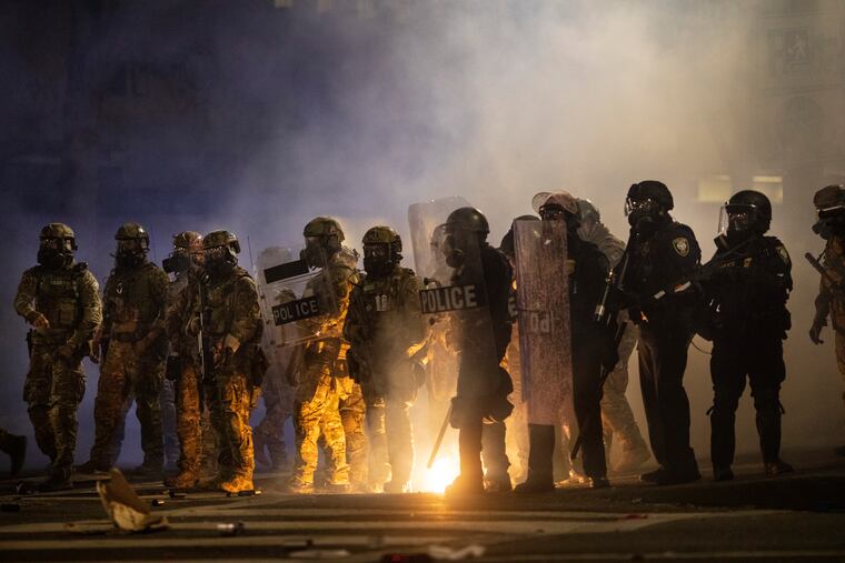 Federal officers and Portland riot police stood in the tear gas while clearing the streets early morning during protests on July 26 in Portland, Ore. Protests have continued.