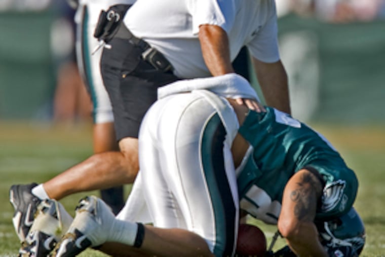 Doubled over in pain, L.J. Smith is attended by defensive line coach Pete Jenkins. The Eagles tight end suffered his injury in a non-contact drill during yesterday's morning practice at Lehigh University.