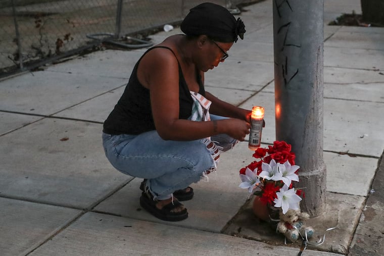 Stacy Satchell lights a candle for her nephew, Da’Juan Brown, 15, at the spot where he was killed in the Kingsessing section of Philadelphia on Wednesday.