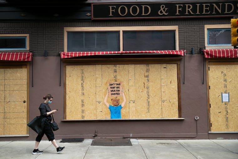 A masked pedestrian walks by a boarded up Food & Friends with a message that says "Don't Take What You Have For Granted" in Center City in April 2020. Businesses are still reeling from closures caused by the pandemic, writes Jabari K. Jones.