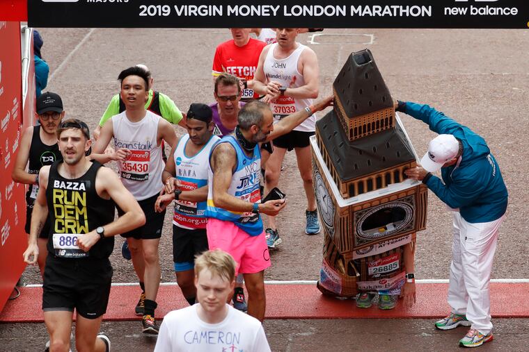 Lukas Bates wearing a costume of the Queen Elizabeth Tower (known as Big Ben) is helped by an official as he attempts to get past the finishing line, during the 39th London Marathon in London, Sunday, April 28, 2019. (AP Photo/Alastair Grant)