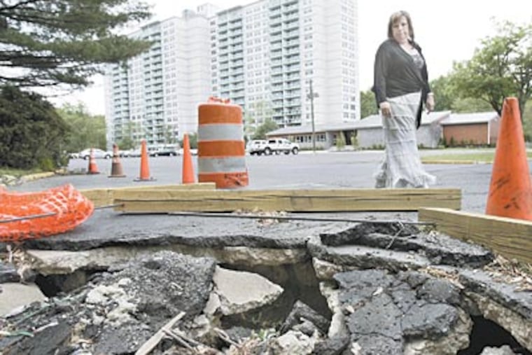 Rae Haltzman, president of the tenants’ association at the Grand Apartment Homes, walks past a sinkhole in the parking lot. (Elizabeth Robertson / Staff Photographer)