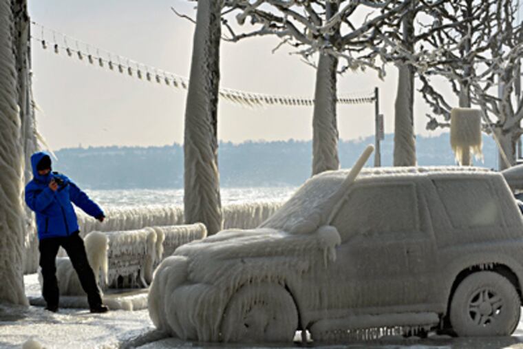 A man takes pictures of an ice-covered car on Lake Geneva's waterside promenade in Versoix, Switzerland. A cold spell with below-zero temperatures has killed scores in Eastern Europe. (Martial Trezzini / Associated Press)
