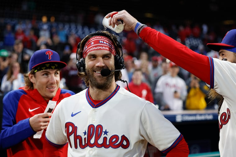 Bryce Harper laughs as teammate Brandon Marsh (right) pours water on Harper with Bryson Stott watching after a win in September.