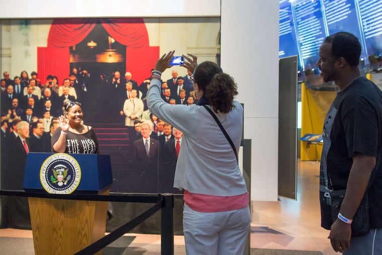 The National Constitution Center, celebrating the document's 227th anniversary, had free admission Wednesday. At the Presidential Oath of Office exhibit, Shawnda Bolden (left) raises her right hand as friends Maria Teresa Del Valle Octavio and Corey Tyrone Jackson capture the moment. New citizens also were sworn in. Story, B6.