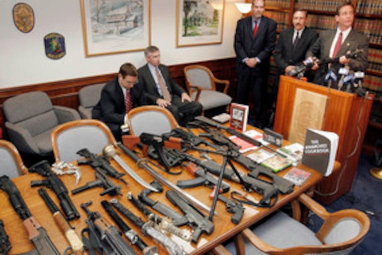 Holding the 9mm weapon that was seized from the home of a 14-year-old boy, Montgomery County District Attorney Bruce L. Castor Jr. displays other objects from the boy's house.
