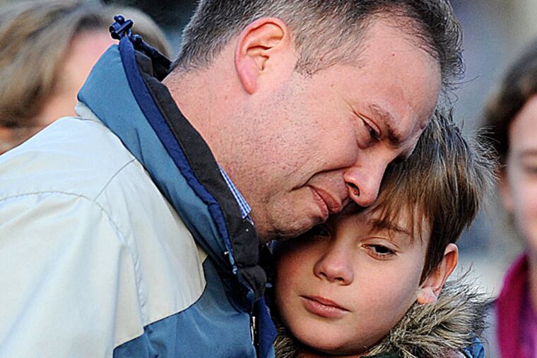 A day after the massacre at Sandy Hook Elementary School, a man holds a child close as they visit a memorial in Newtown, Conn., that mourners created nearby. OLIVIER DOULIERY / Abaca Press, MCT
