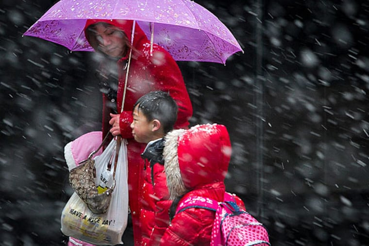 Pink and red contrast against the charcoal of the building and the white of the falling show as a woman leads the way along Eighth Street near Filbert Street in Philadelphia. (Alejandro A. Alvarez/Staff)
