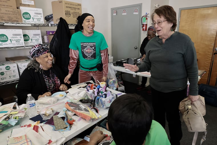 Pan-African Sisterhood Health Initiative (P.A.S.H.I.) co-founder Maisha Sullivan-Ongoza (seated at left), her daughter Milele Sullivan (center) and first-time volunteer Judy Watman of Narberth (standing at right) laugh at a joke one of the women made at the Ujima Friends Peace Center in Philadelphia on Wednesday, January 15, 2025.