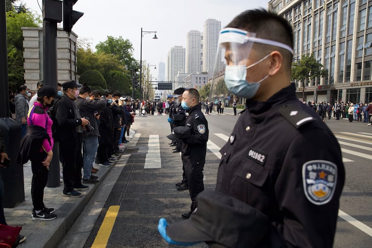 People and policemen bow their heads during a national moment of mourning for victims of coronavirus in Wuhan in central China's Hubei Province, Saturday, April 4, 2020. With air raid sirens wailing and flags at half-staff, China on Saturday held a three-minute nationwide moment of reflection to honor those who have died in the coronavirus outbreak, especially "martyrs" who fell while fighting what has become a global pandemic.