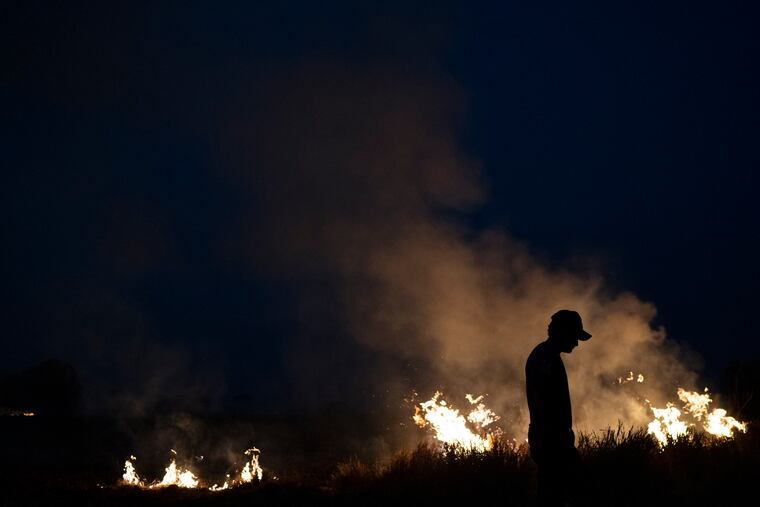 Neri dos Santos Silva, center, is silhouetted against an encroaching fire threat after he spent hours digging trenches to keep the flames from spreading to the farm he works on, in the Nova Santa Helena municipality, in the state of Mato Grosso, Brazil, Friday, Aug. 23, 2019. Under increasing international pressure to contain fires sweeping parts of the Amazon, Brazilian President Jair Bolsonaro on Friday authorized use of the military to battle the massive blazes.
