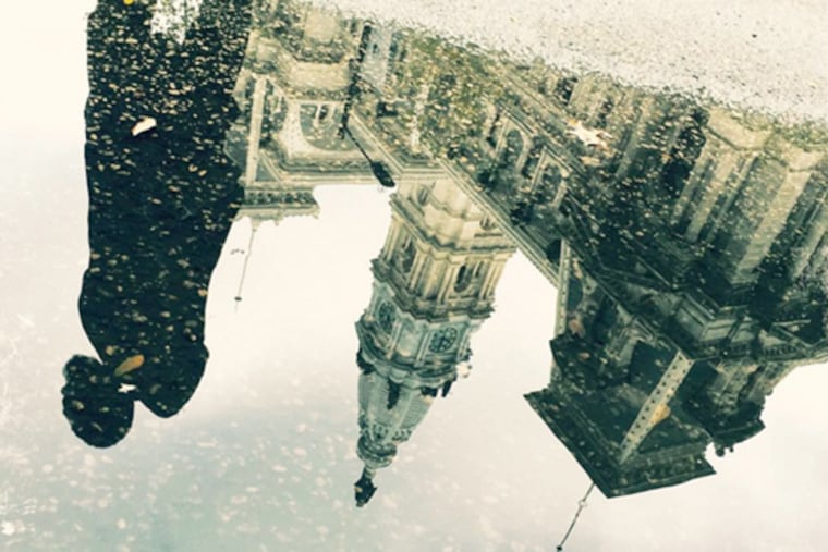 A man's image is reflected in a puddle in front of City Hall in Pennsylvania.